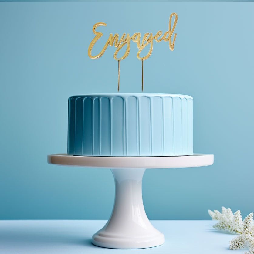 Gold "Engaged" cake topper from Cake and Candle giftware, featuring elegant script designed for wedding or engagement cakes.